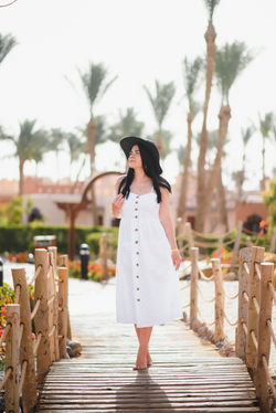 White button-front midi sundress with a black sun hat, walking on a boardwalk