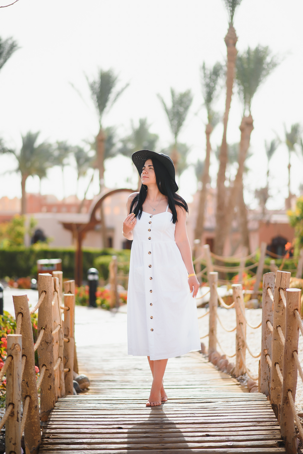 White button-front midi sundress with a black sun hat, walking on a boardwalk
